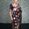 A black silk saree with silver geometric and floral patterns and a gold border.